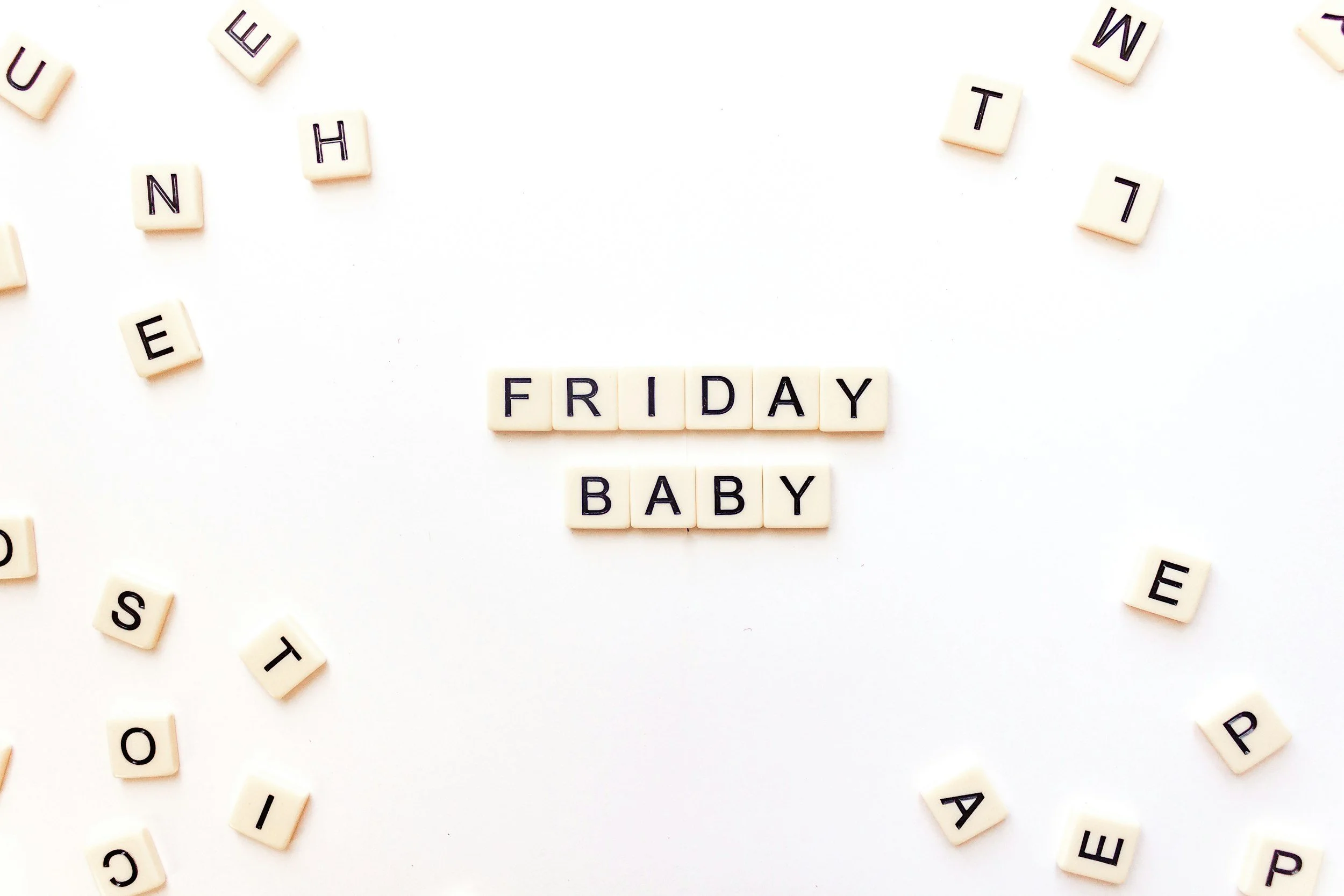 Scrabble tiles spell out "FRIDAY BABY" on a white background, with scattered letter tiles around them.