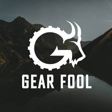 A logo with a mountain landscape background, featuring a mechanical gear with a goat's head illustration and the text 'GEAR FOOL' underneath.