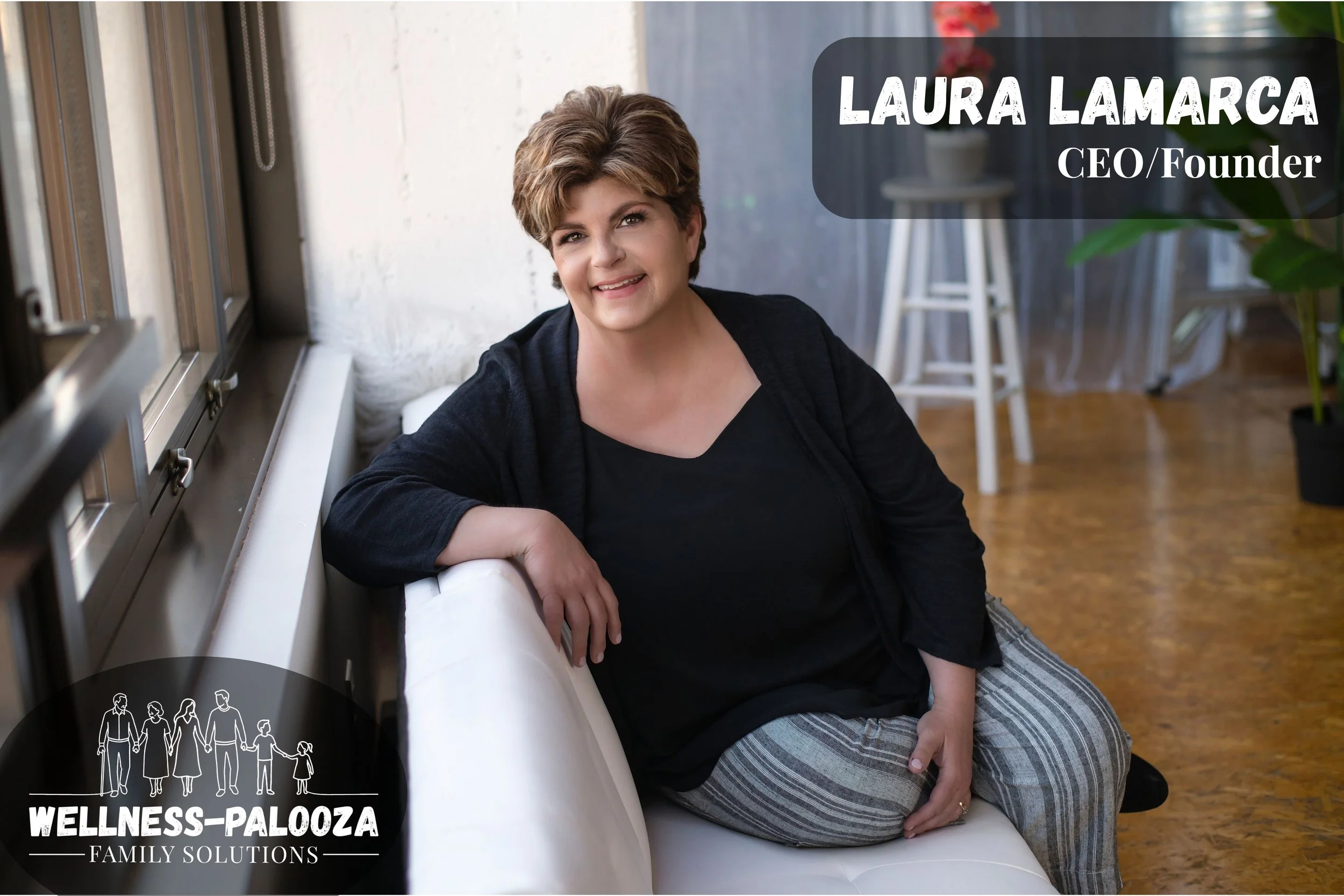 A woman with short hair smiling, sitting on the floor next to a large pipe in an indoor space with a wooden floor and plants, with a label indicating she is Laura Lamarca, CEO/Founder of Wellness-Palooza.