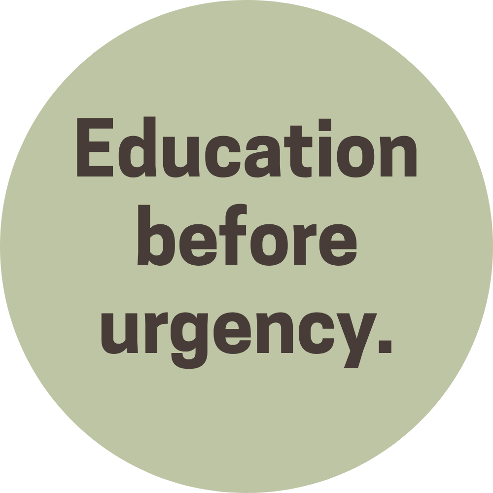 A circular sign with a pale green background and black text that reads "Education before urgency."