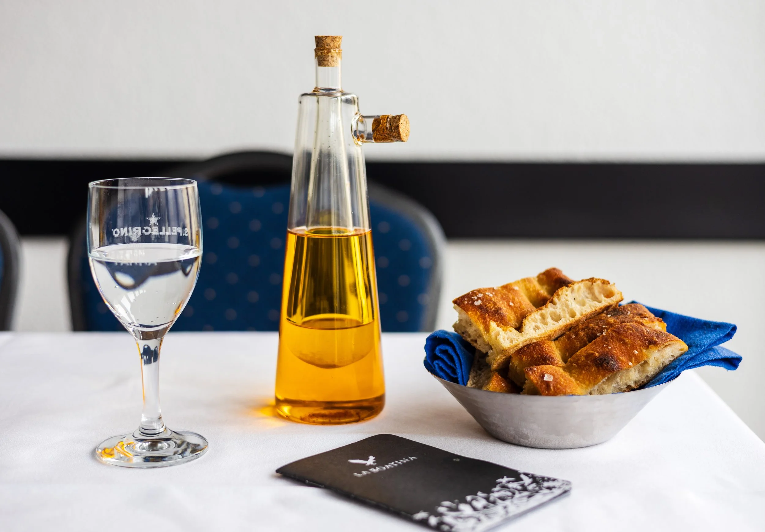 Frisch gebackenes Brot mit Olivenöl und einem Glas Wasser auf einem Restauranttisch.