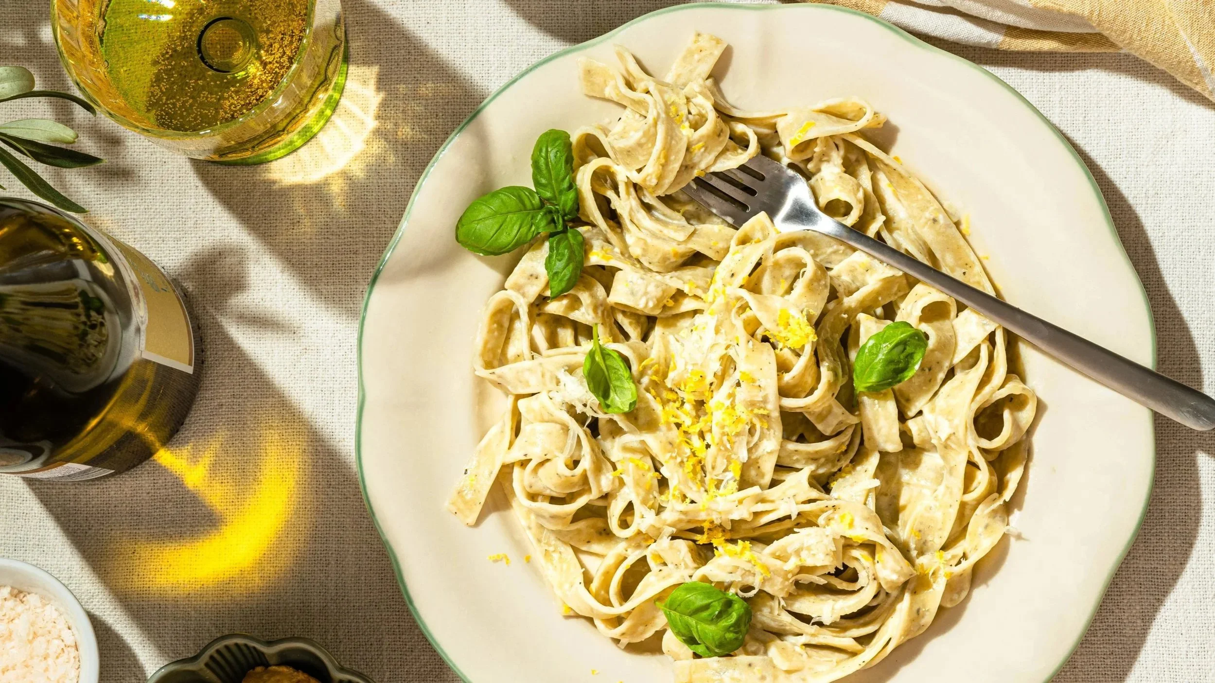 Tagliatelle mit cremiger Zitronensauce und Basilikum auf einem sommerlich gedeckten Tisch.