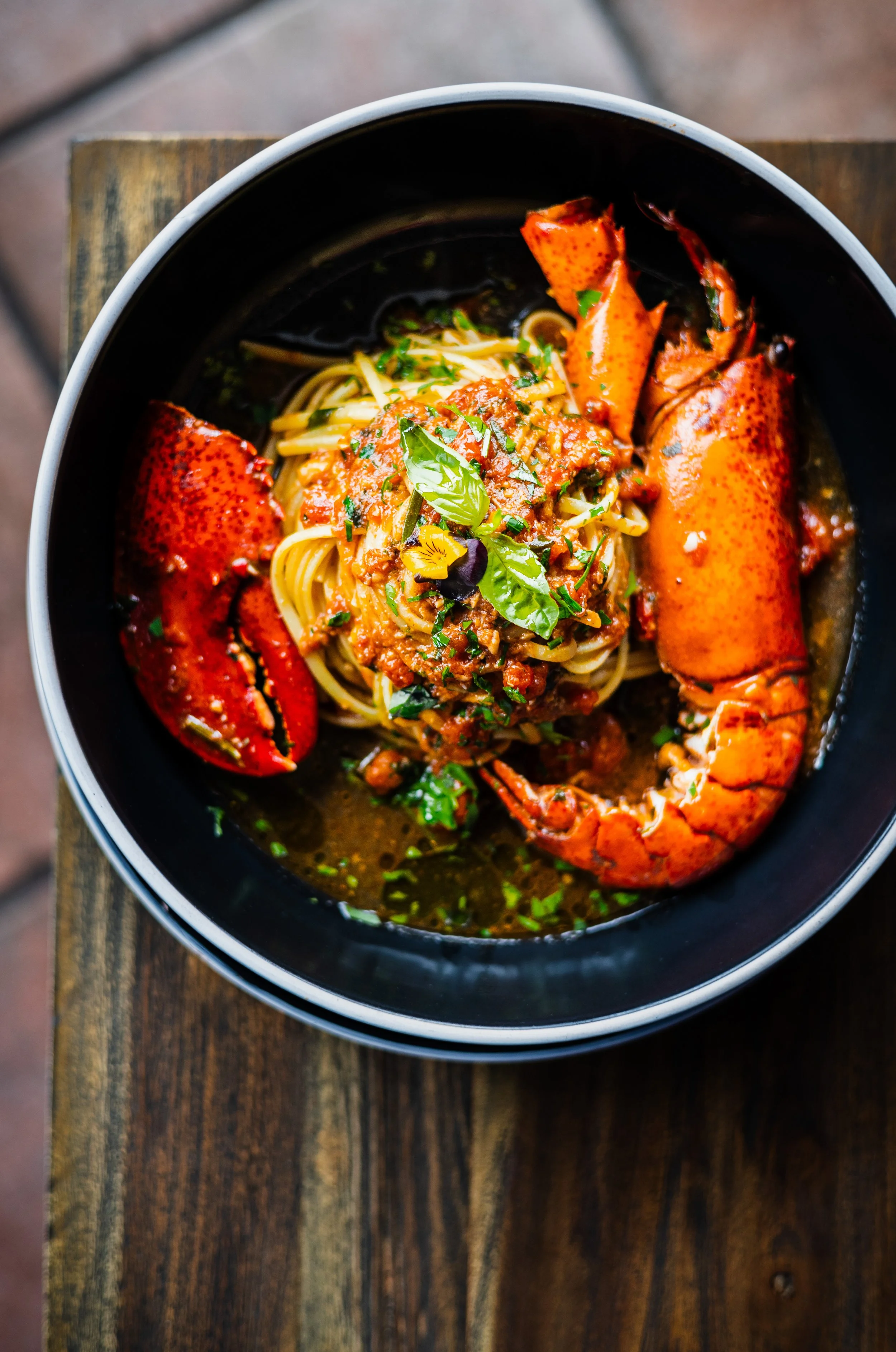 Lobster-Nudeln in einer schwarzen Schüssel, garniert mit frischen Kräutern, auf einem Holztisch