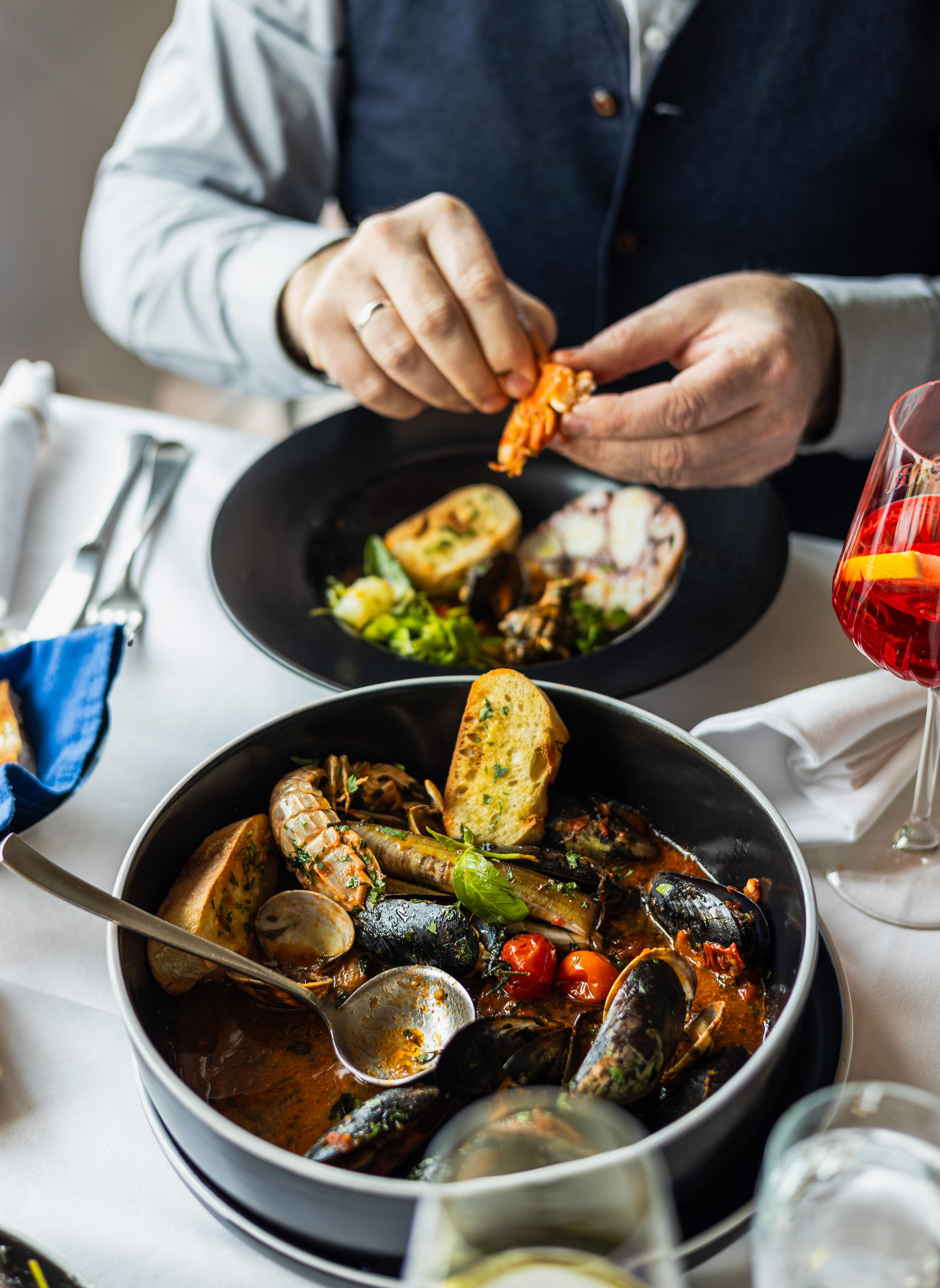 Ein Teller mit Meeresfrüchtesuppe, darunter verschiedene frische Meeresfrüchte, Tomaten und Brot, serviert auf einem Restauranttisch.