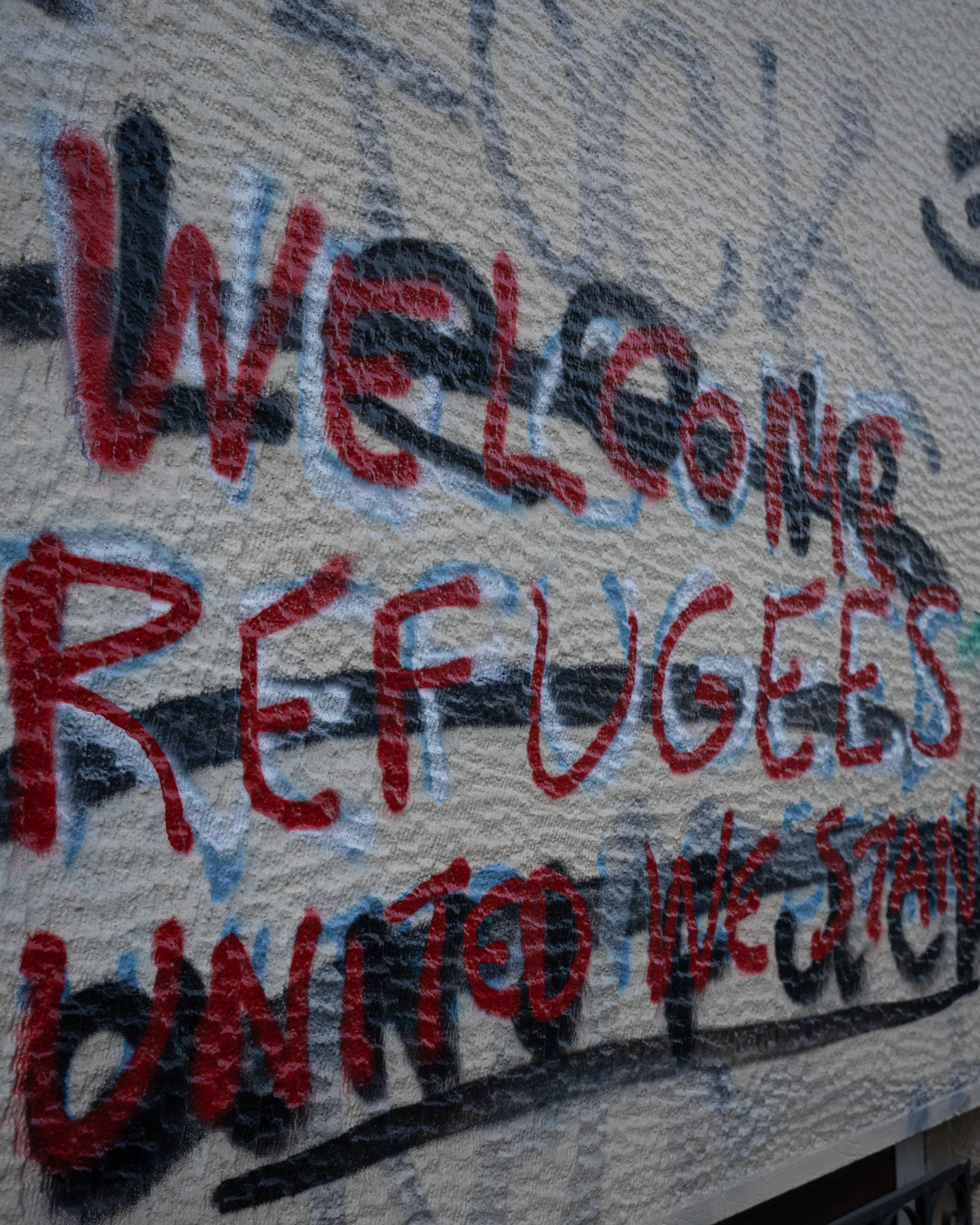 Close-up of a wall with graffiti featuring overlapping red, black, blue, and white spray-painted text and symbols.
