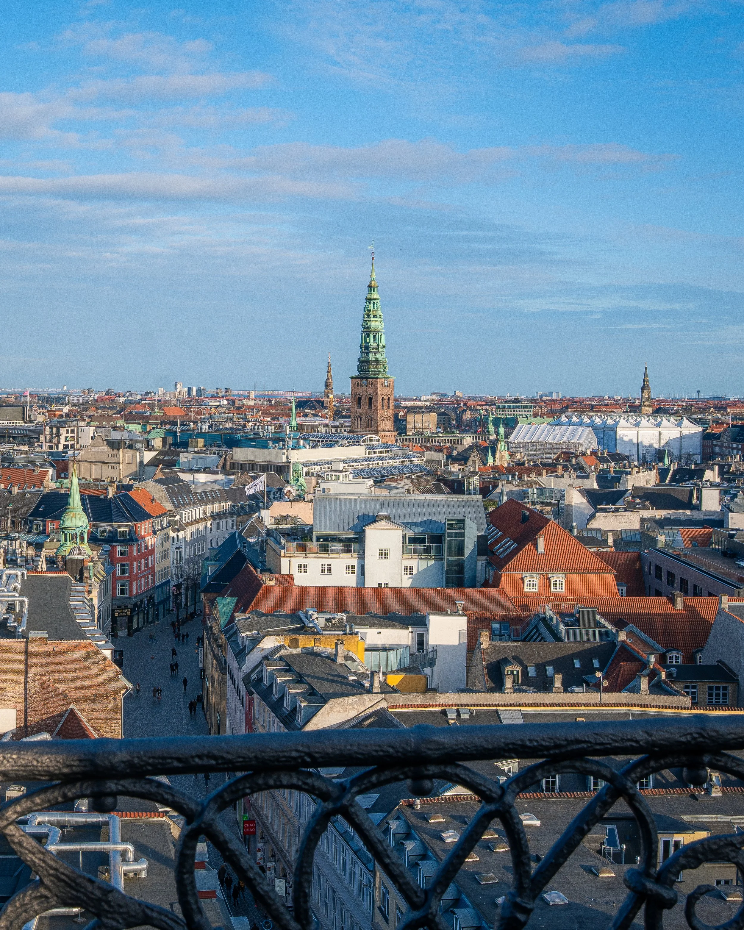 Cityscape view of historical buildings with prominent tall church steeples under a partly cloudy sky, seen from a high vantage point overlooking the city.