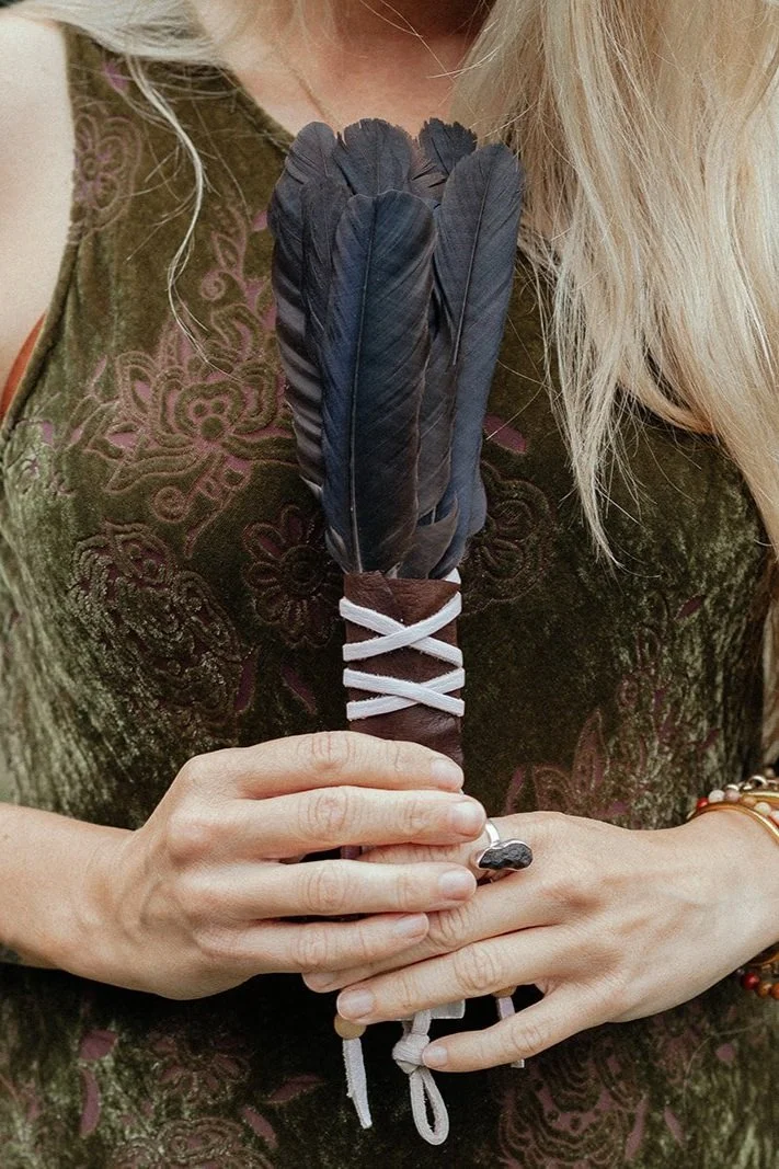 Person holding a bundle of large black feathers tied with white string, wearing a green patterned dress.