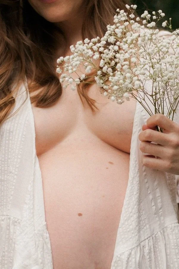 A woman holding a bouquet of white baby's breath flowers, partially undressed with an open white garment, visible chest and midriff