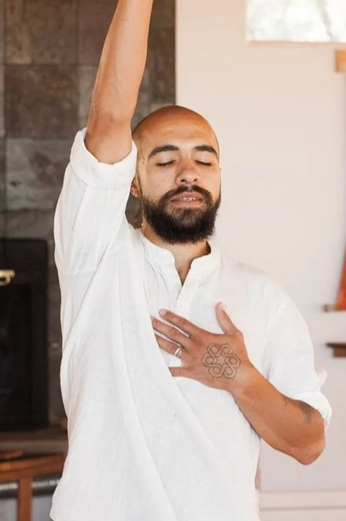 A man practicing yoga with one arm raised and his hand on his chest, eyes closed in a peaceful expression.