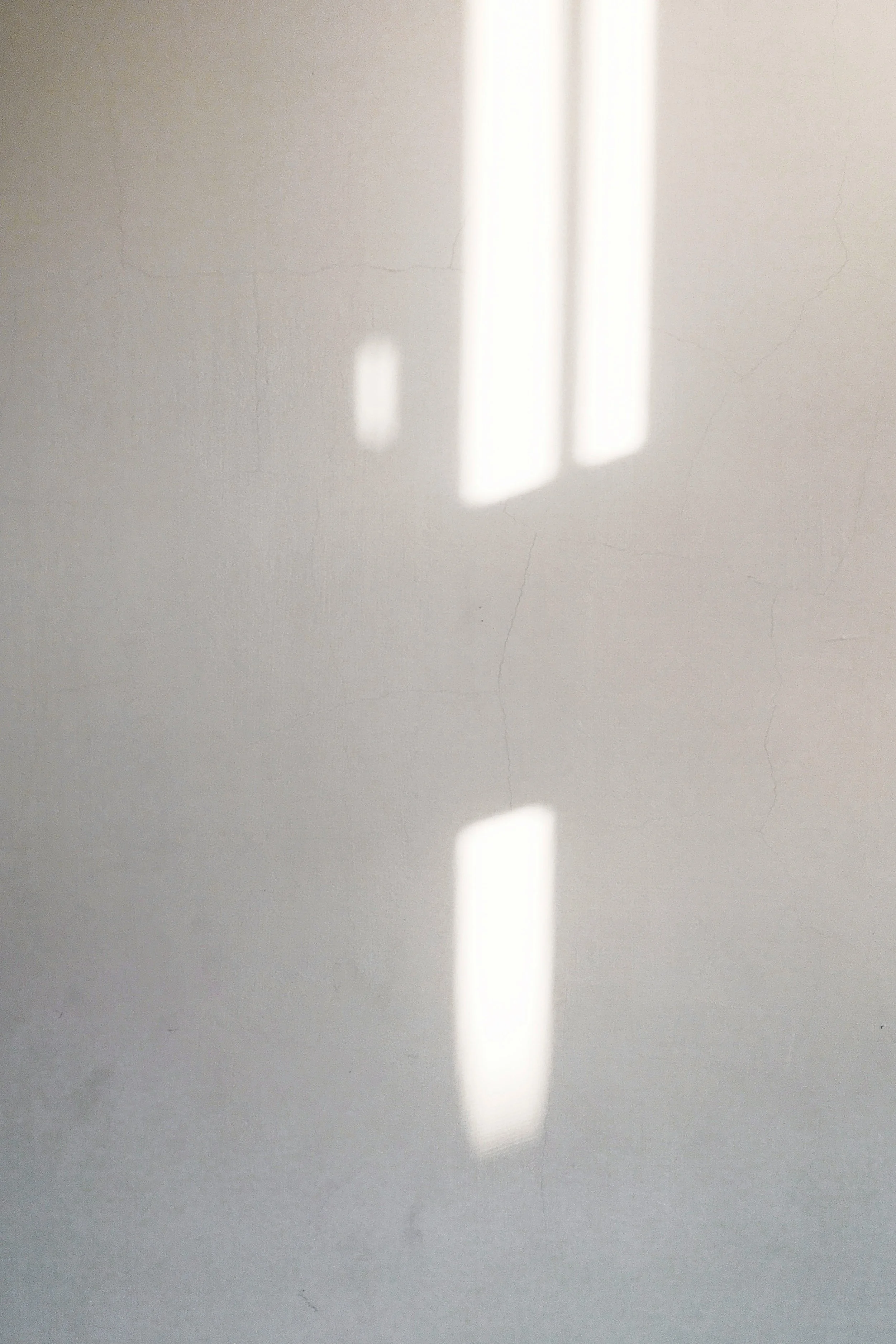 Sunlight shining through window creating rectangular light reflections on a plain white wall.