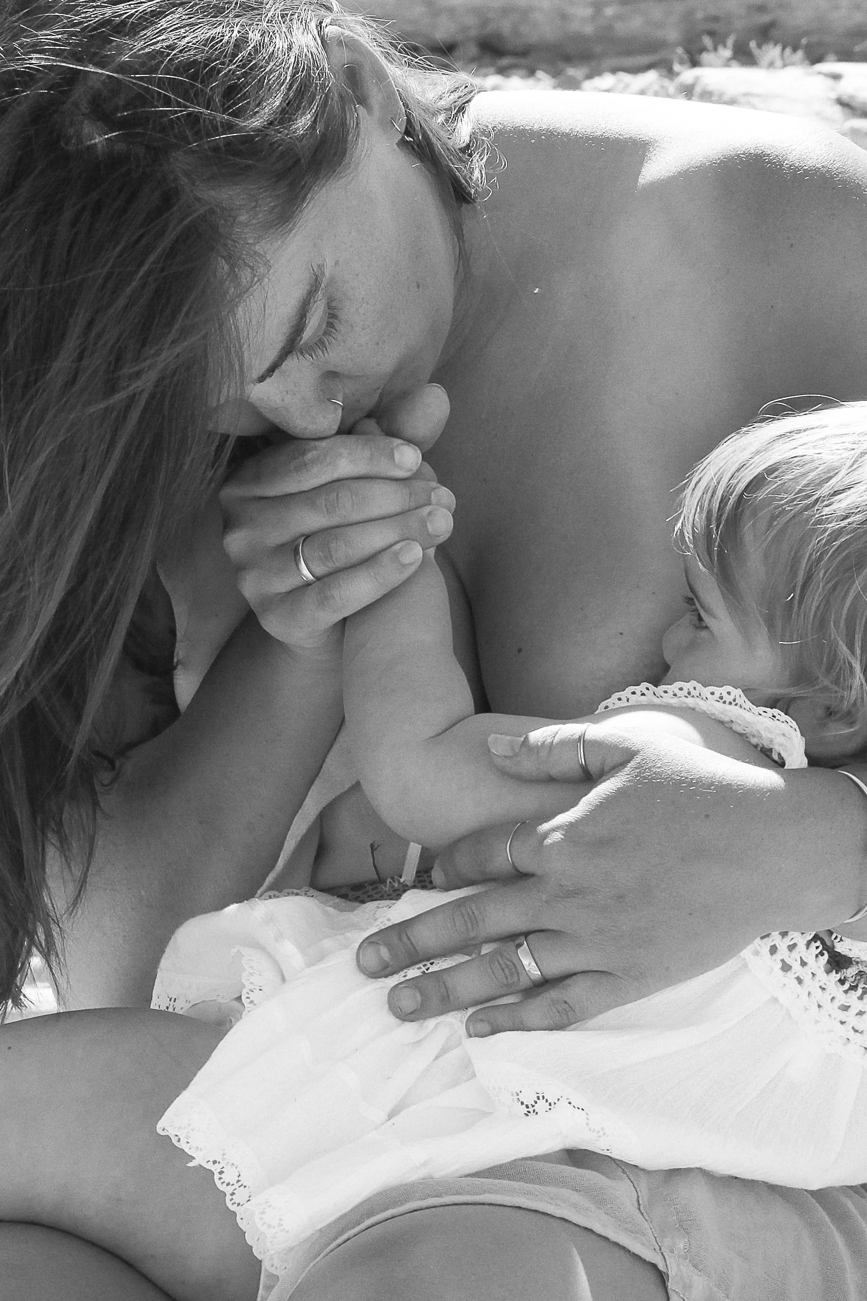 A woman, a child, and an adult holding hands during breastfeeding outdoors in black and white.