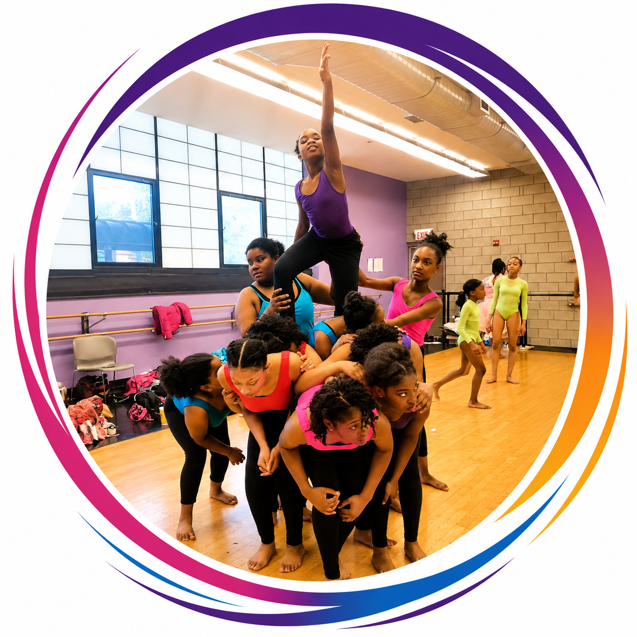 A group of young girls practicing acro yoga or a similar activity in a dance studio, with one girl balancing on top of others who are supporting her in a pyramid formation.
