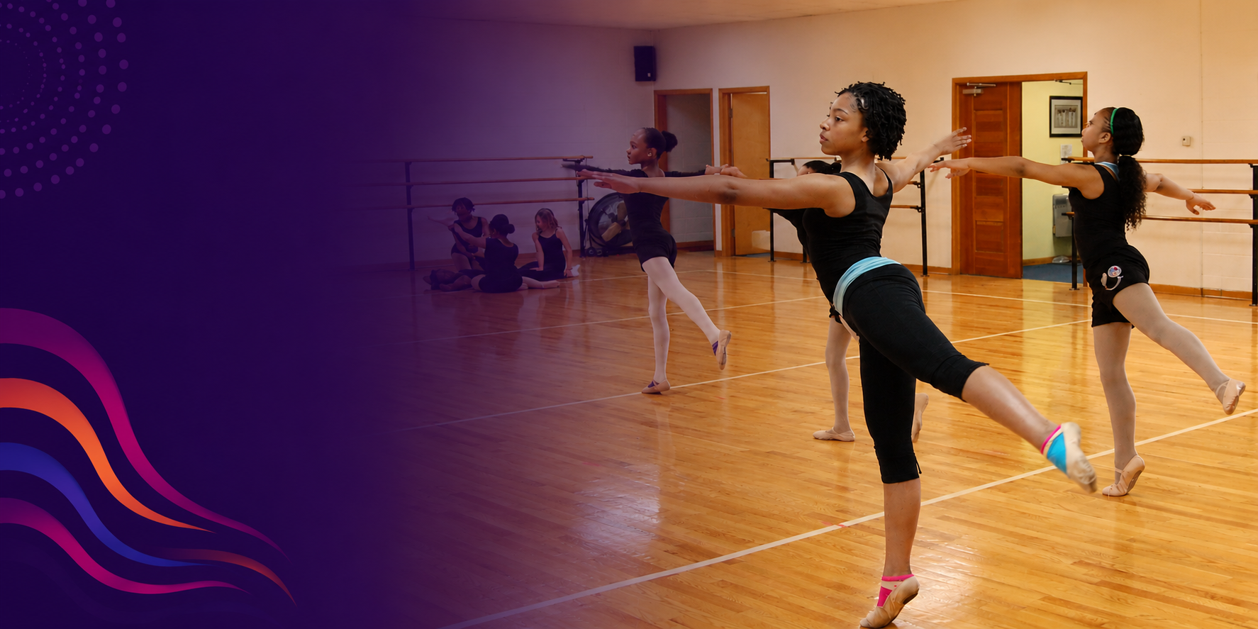 Ballet dancers practicing in a dance studio with wooden floors and mirrors, some dancers sitting on the floor, others stretching and dancing at the barre.