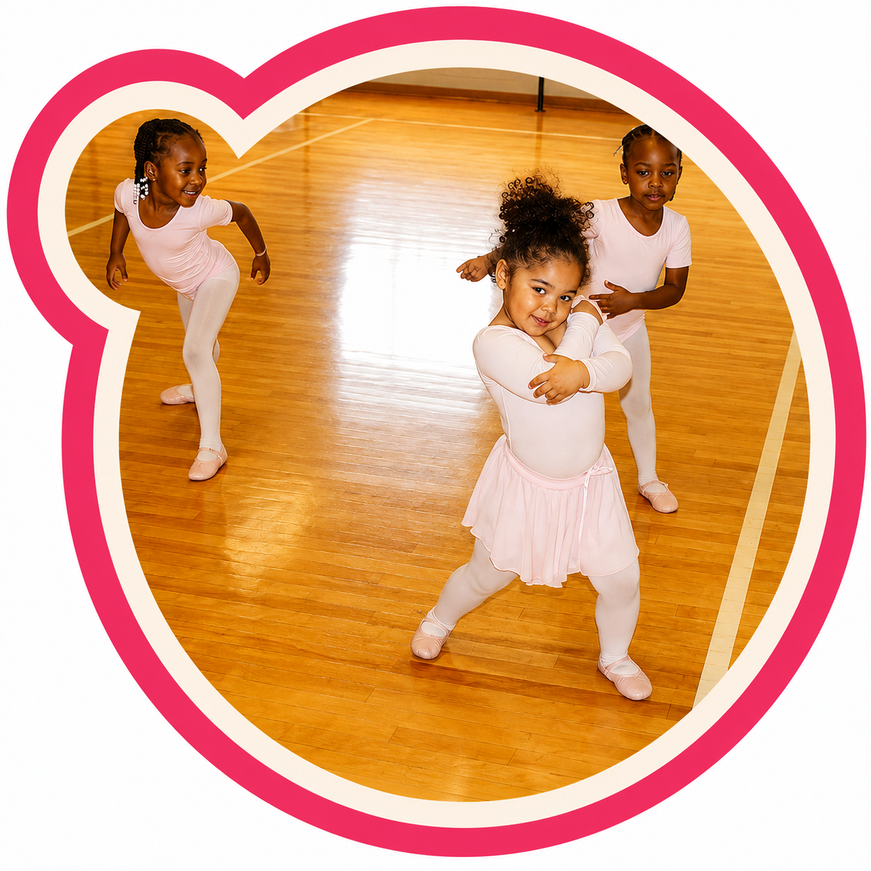Three young girls in ballet outfits practicing dance moves in a gymnasium, framed by a pink heart outline.