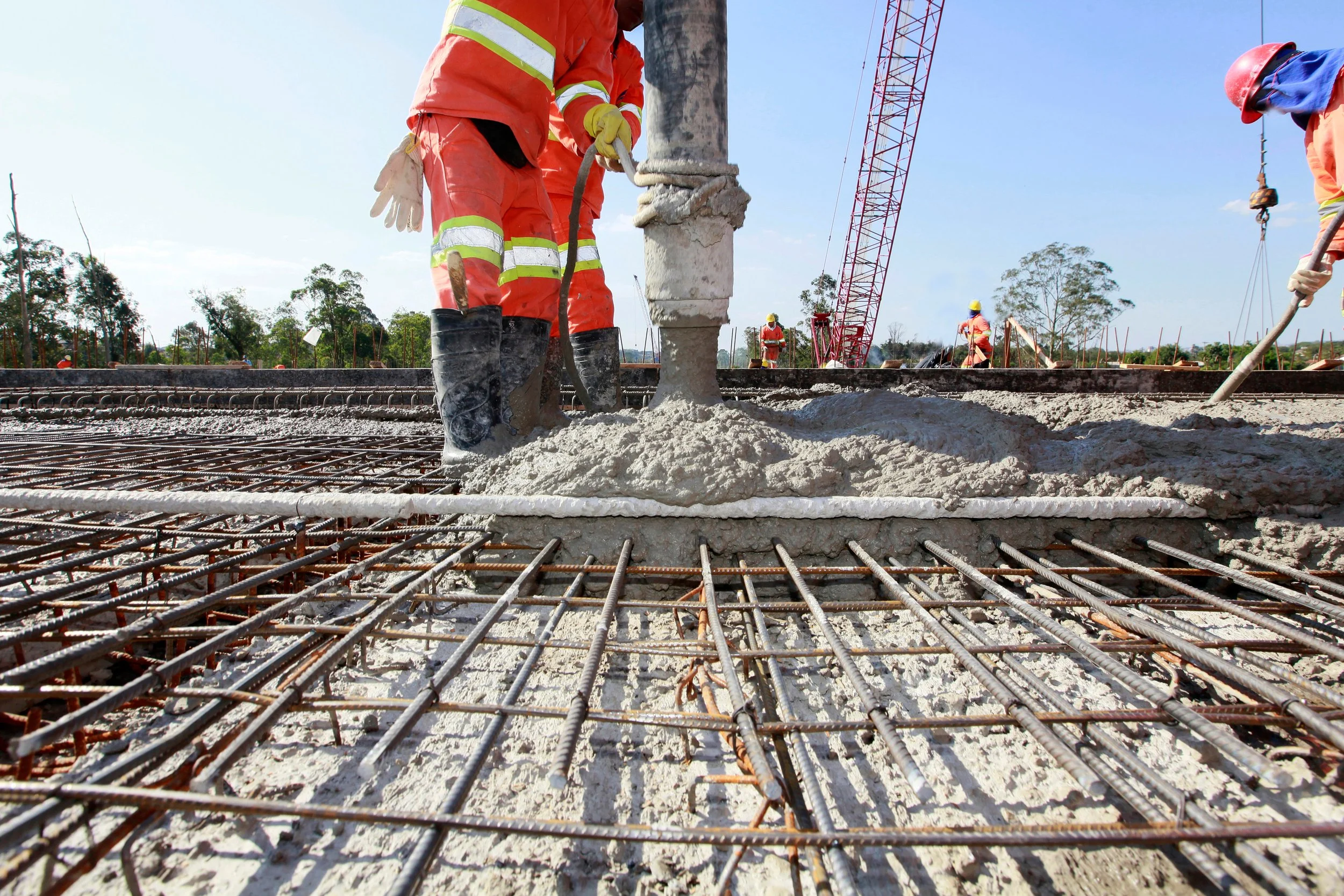 Construction workers pour concrete over a steel reinforcing grid at an active infrastructure construction site.