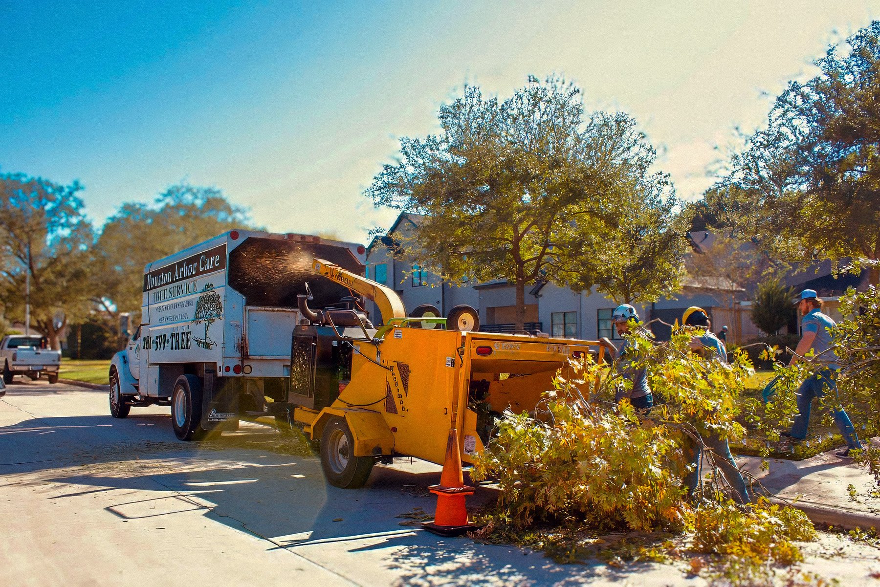 Tree crew feeding brush into a chipper beside the truck at a job site