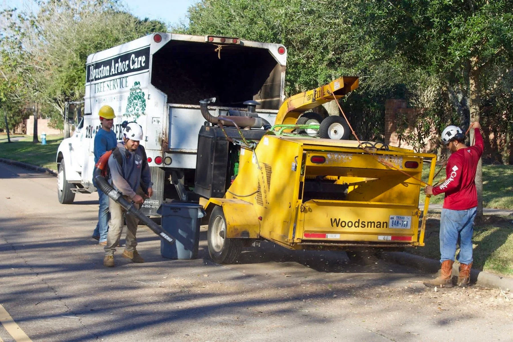 Crew chipping branches behind the Houston Arbor Care truck on a residential street