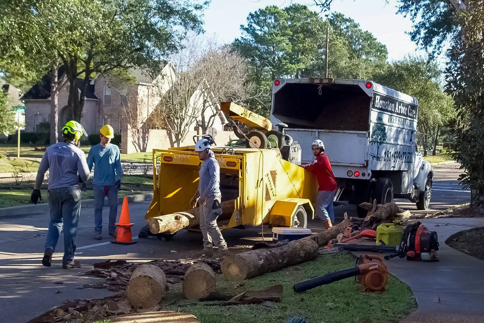 Houston Arbor Care crew in hard hats clearing storm-downed logs and chipping brush on a residential street