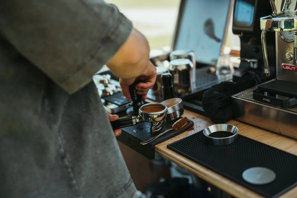 Barista preparing espresso shot at a coffee station with espresso machine, grinder, and coffee accessories.