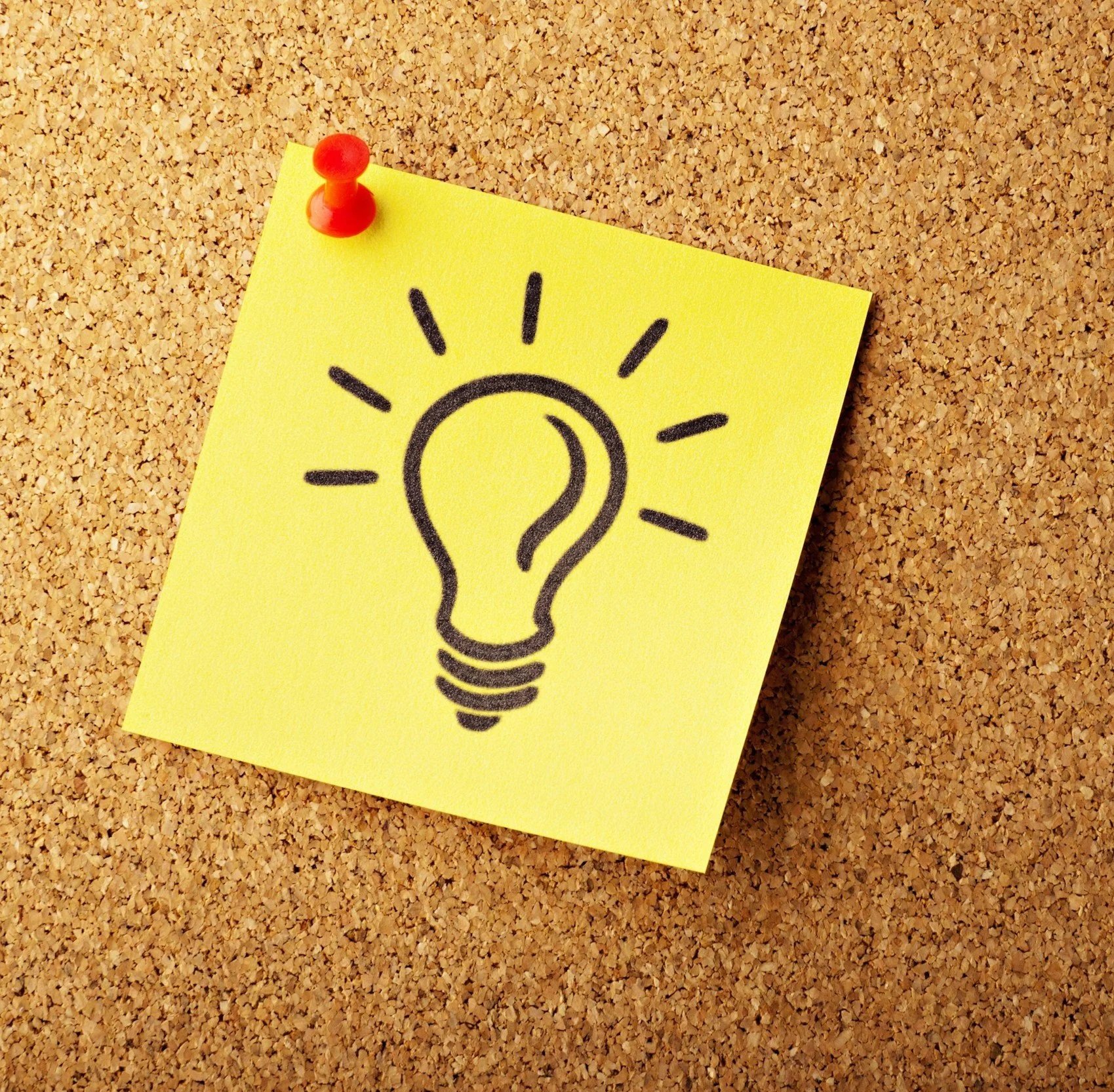 A yellow sticky note with a black outline drawing of a light bulb, pinned to a cork board with a red thumbtack.