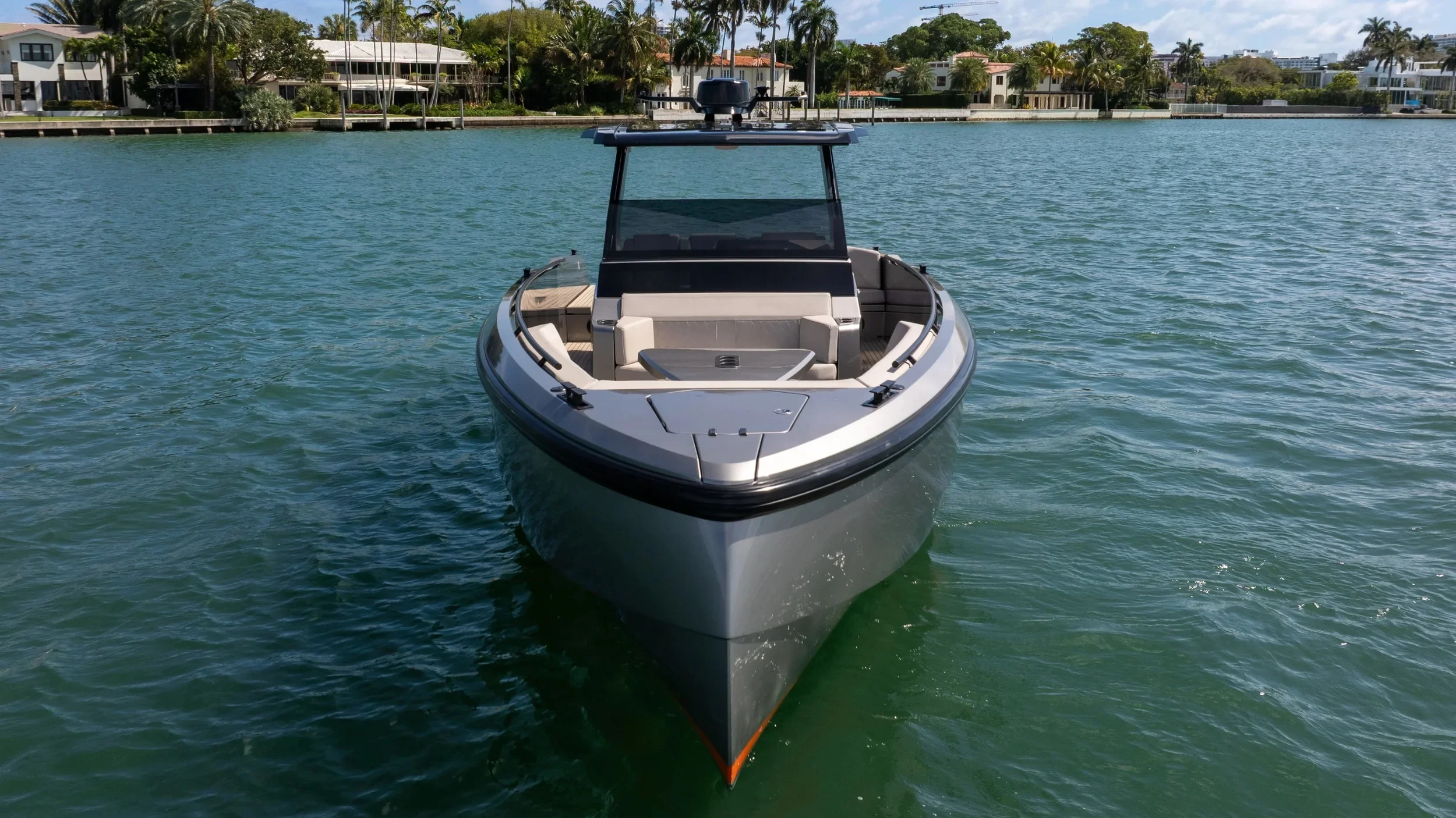 A modern motorboat on the water with residential houses and palm trees in the background.