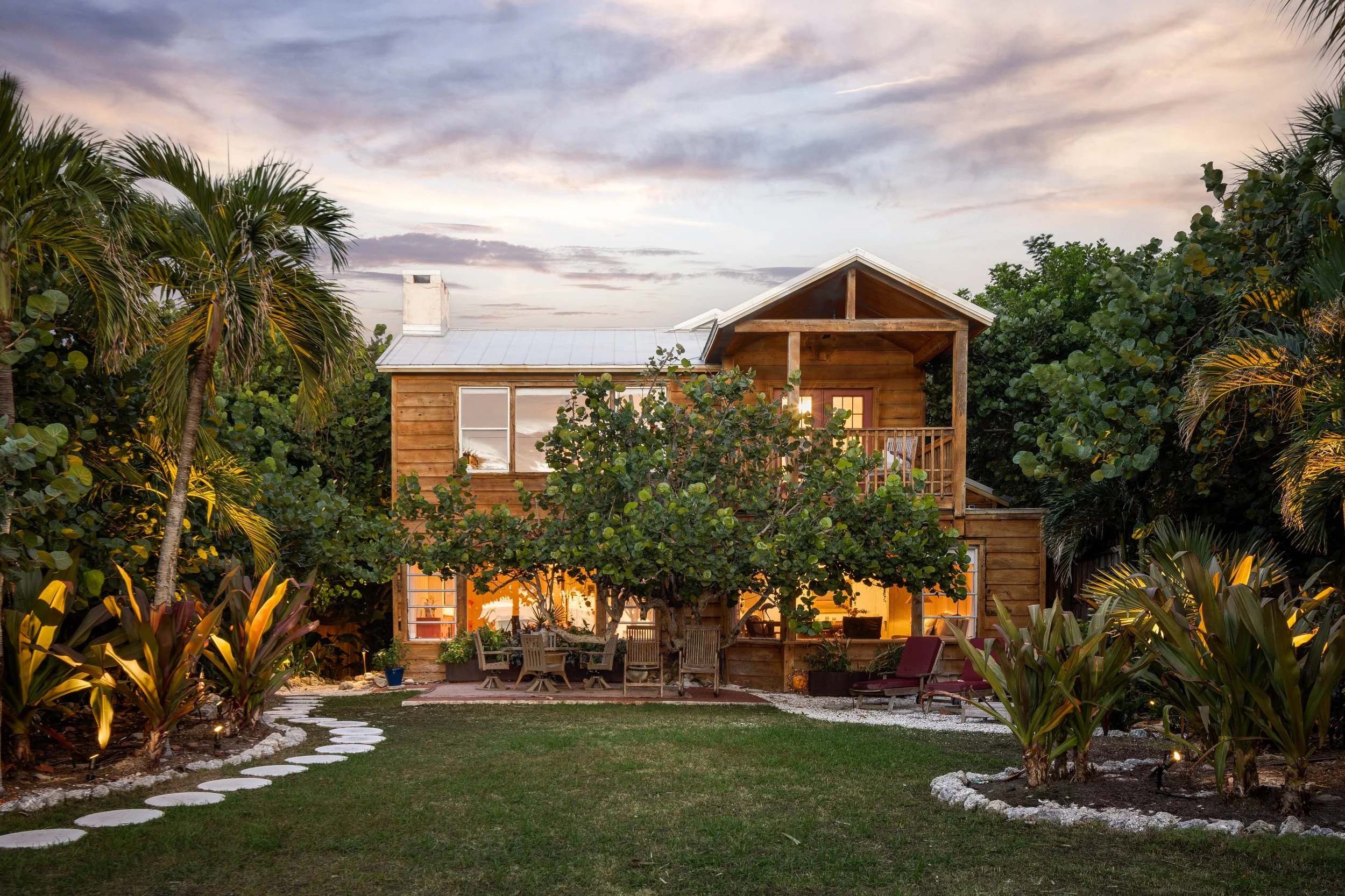 A two-story wooden house with a backyard, surrounded by various green trees and plants, with a pathway made of stepping stones leading to the house. Original Beach House, Siesta Key, Florida