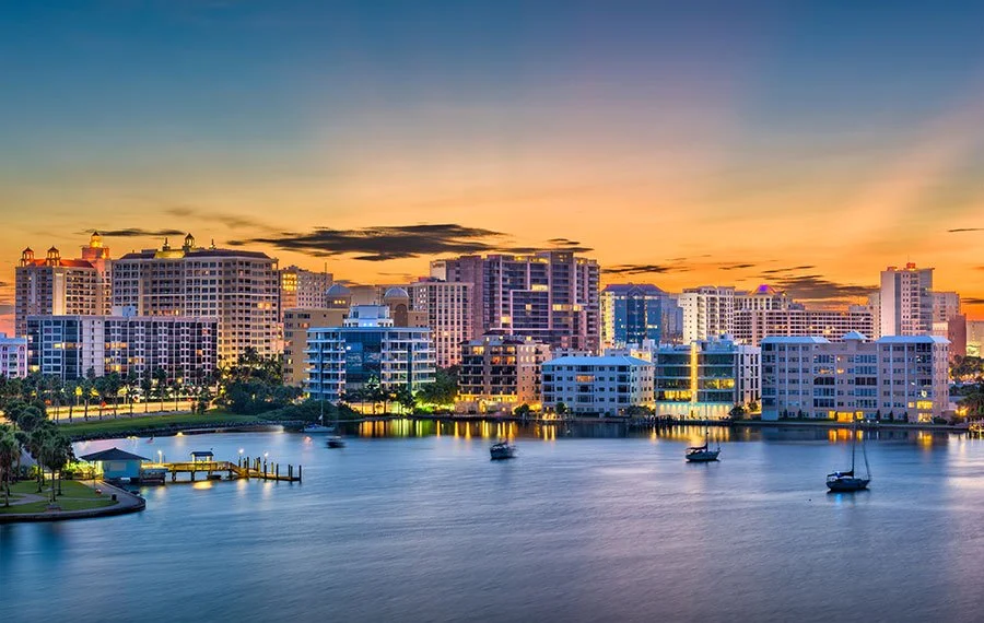 Skyline of modern high-rise buildings along a waterfront with boats, at sunset with colorful sky.
