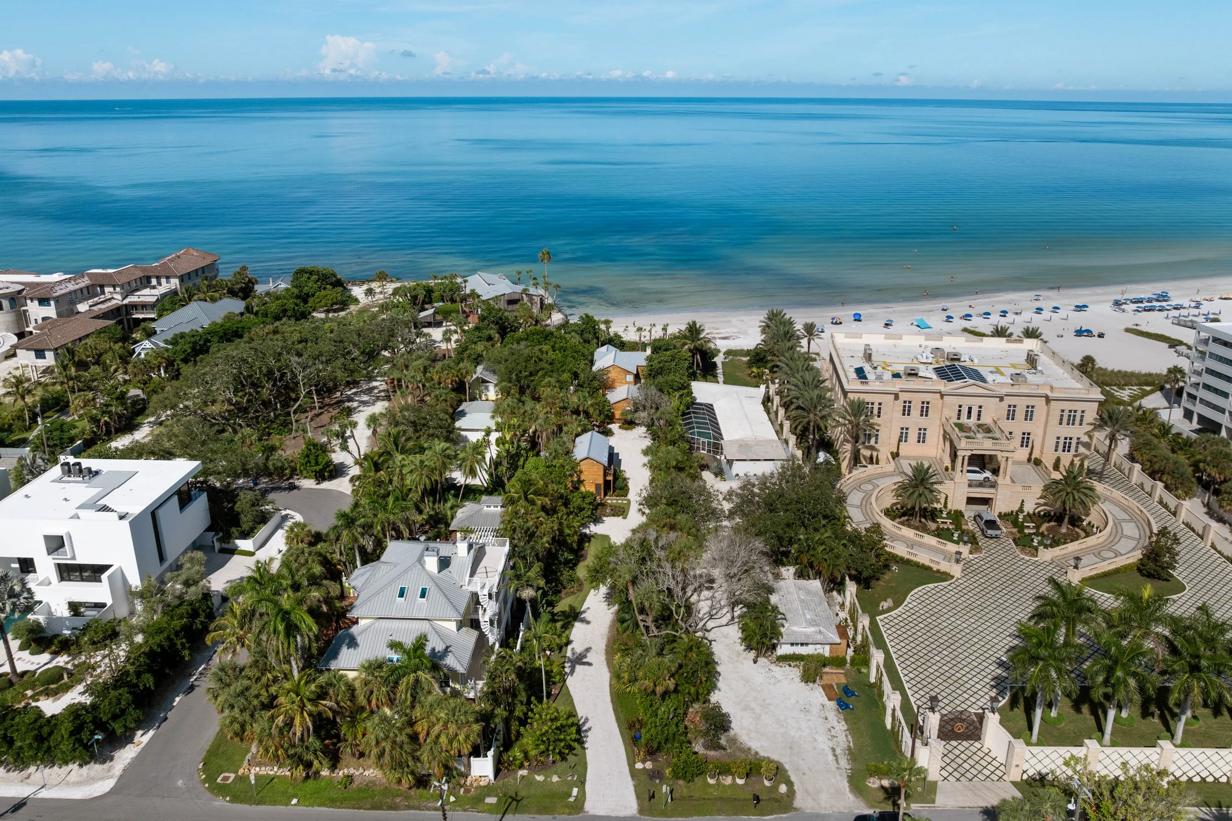 Aerial view of beachfront properties with lush greenery, a sandy beach, and calm ocean waters under a partly cloudy sky. Original Beach House, Siesta Key, Florida