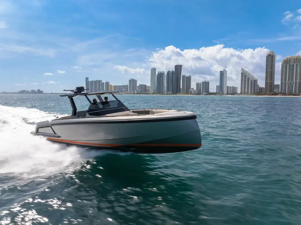 A speedboat on the water with a city skyline in the background on a sunny day.