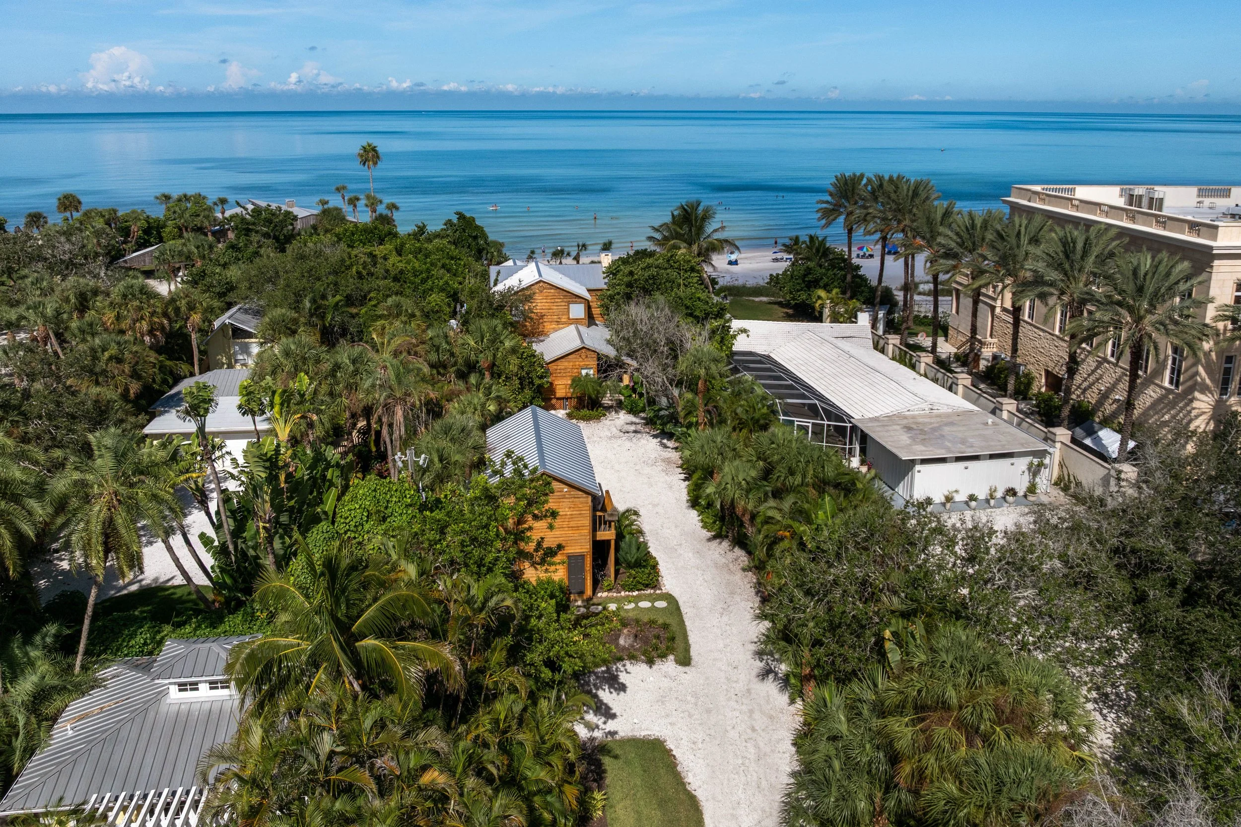 Aerial view of a tropical beach with lush greenery, houses, and palm trees leading to the ocean with small waves and a clear blue sky. Original Beach House, Siesta Key, Florida