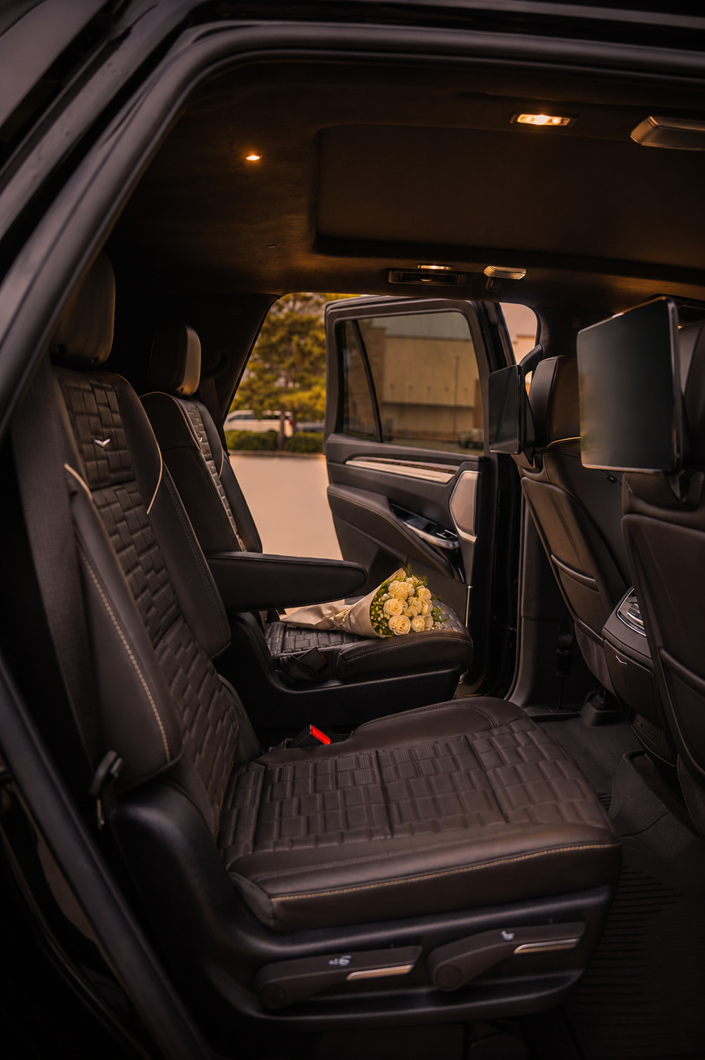 Inside a black luxury car with black leather seats, a bouquet of white roses rests on the seat, suggesting a special occasion or event.