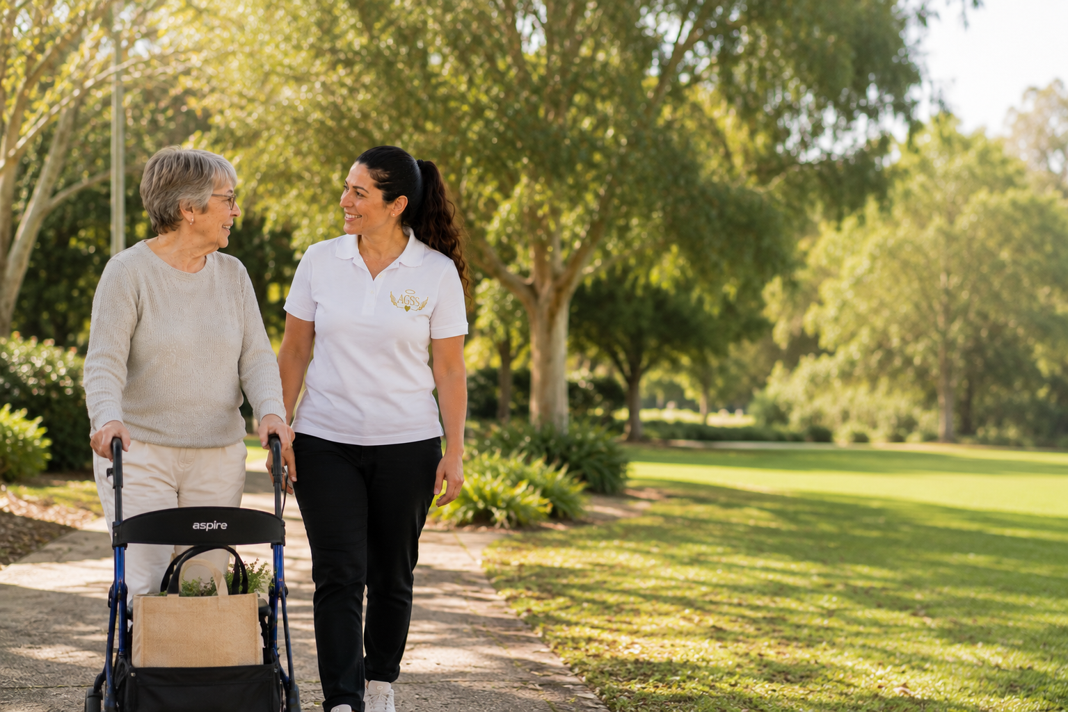 An elderly woman with gray hair walking with a caregiver in a park on a sunny day.