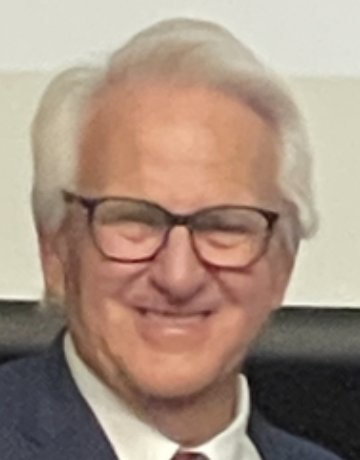 An elderly man with white hair and glasses, smiling.