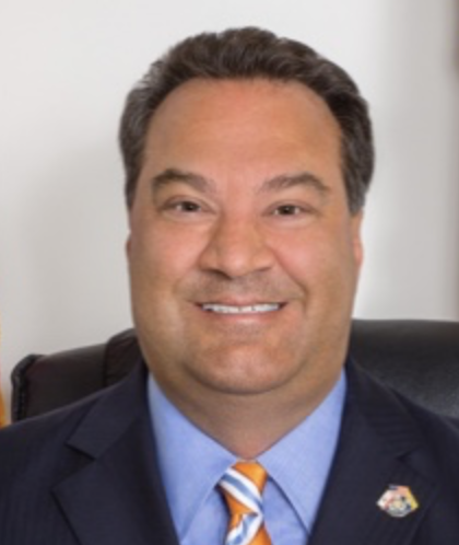 A smiling man in a suit and tie sitting in an office chair.