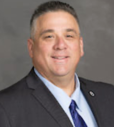 Professional headshot of a man in a suit and tie, smiling.