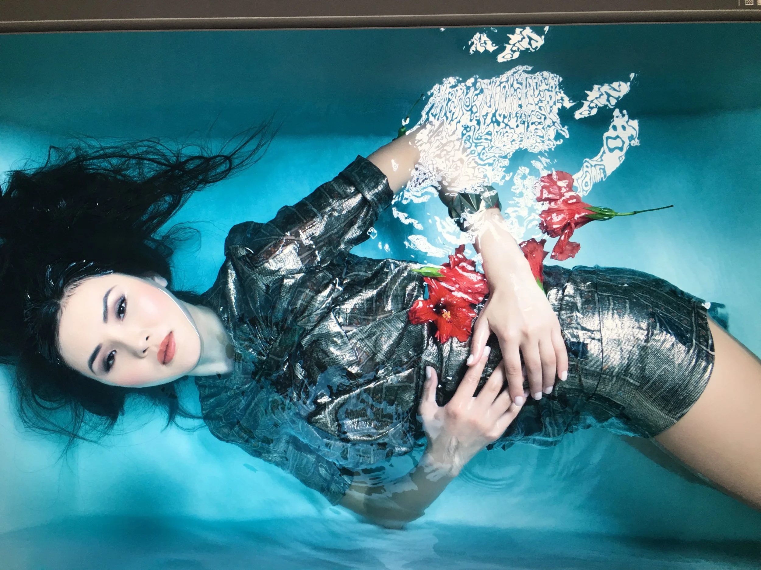 A woman with long black hair lying in a field of blue. The image is distorted with white outlines and patterns, and she has a flower in her hand.