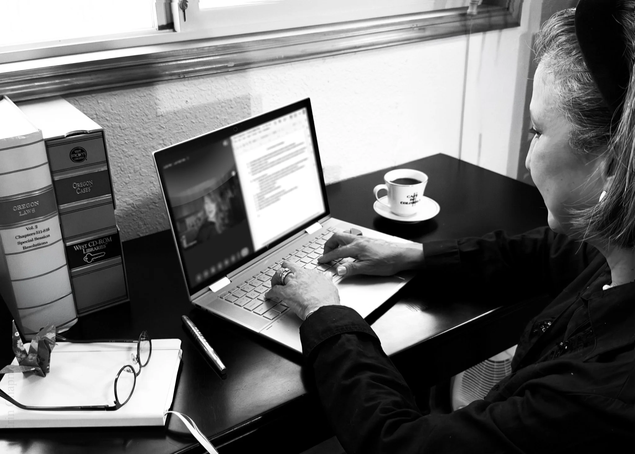 Woman typing on a laptop at a desk beside law books and a cup of coffee