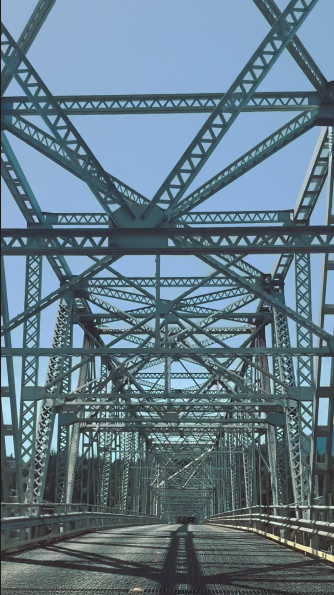 View down the roadway of a steel truss bridge under a clear blue sky