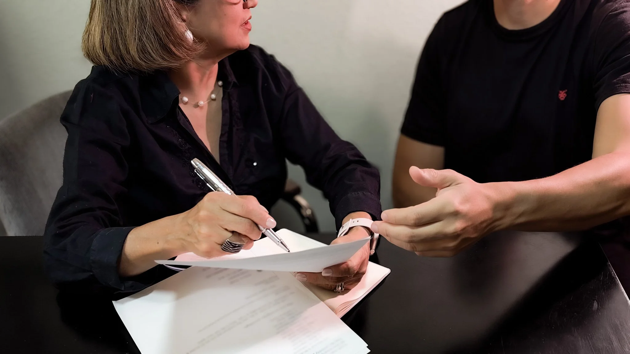 Woman signing paperwork at a table while a man gestures beside her