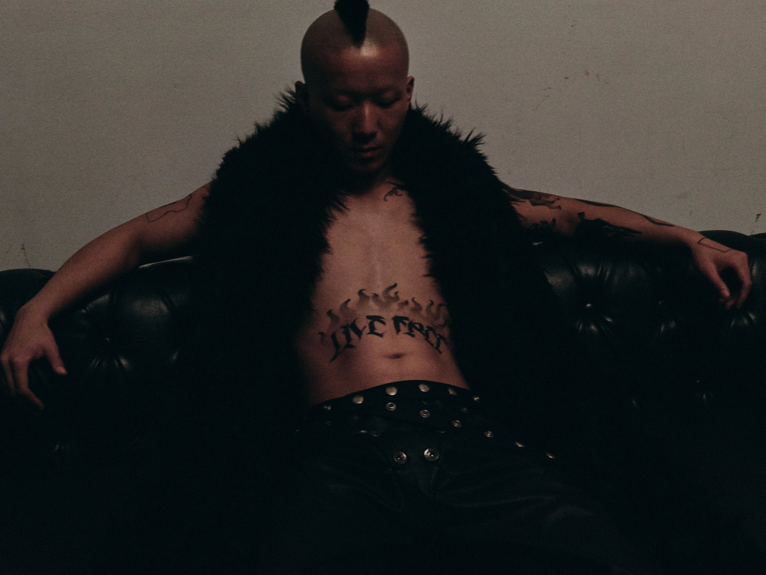 A person with a mohawk hairstyle, shirtless, and tattoos on the arms, sitting on a black leather couch with arms outstretched, in a dimly lit room.
Studio projects of Asian Life by Photographer Ian O'Hara

