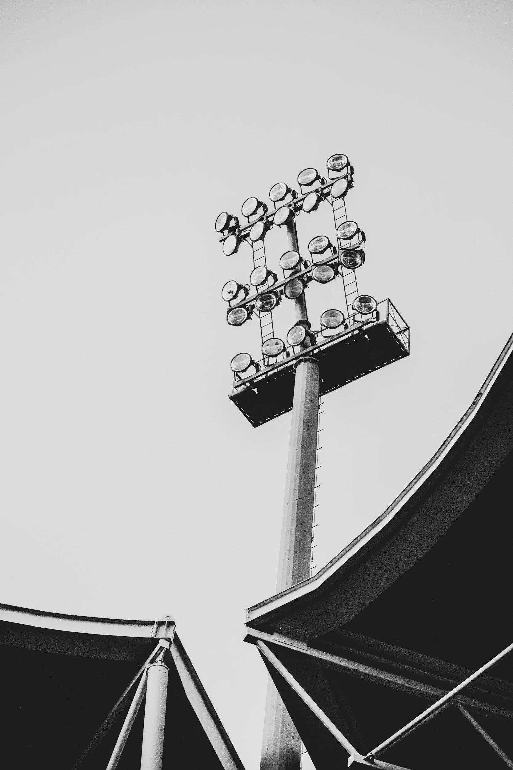 Black and white photo of stadium floodlights attached to tall poles, viewed upward from beneath the structures.