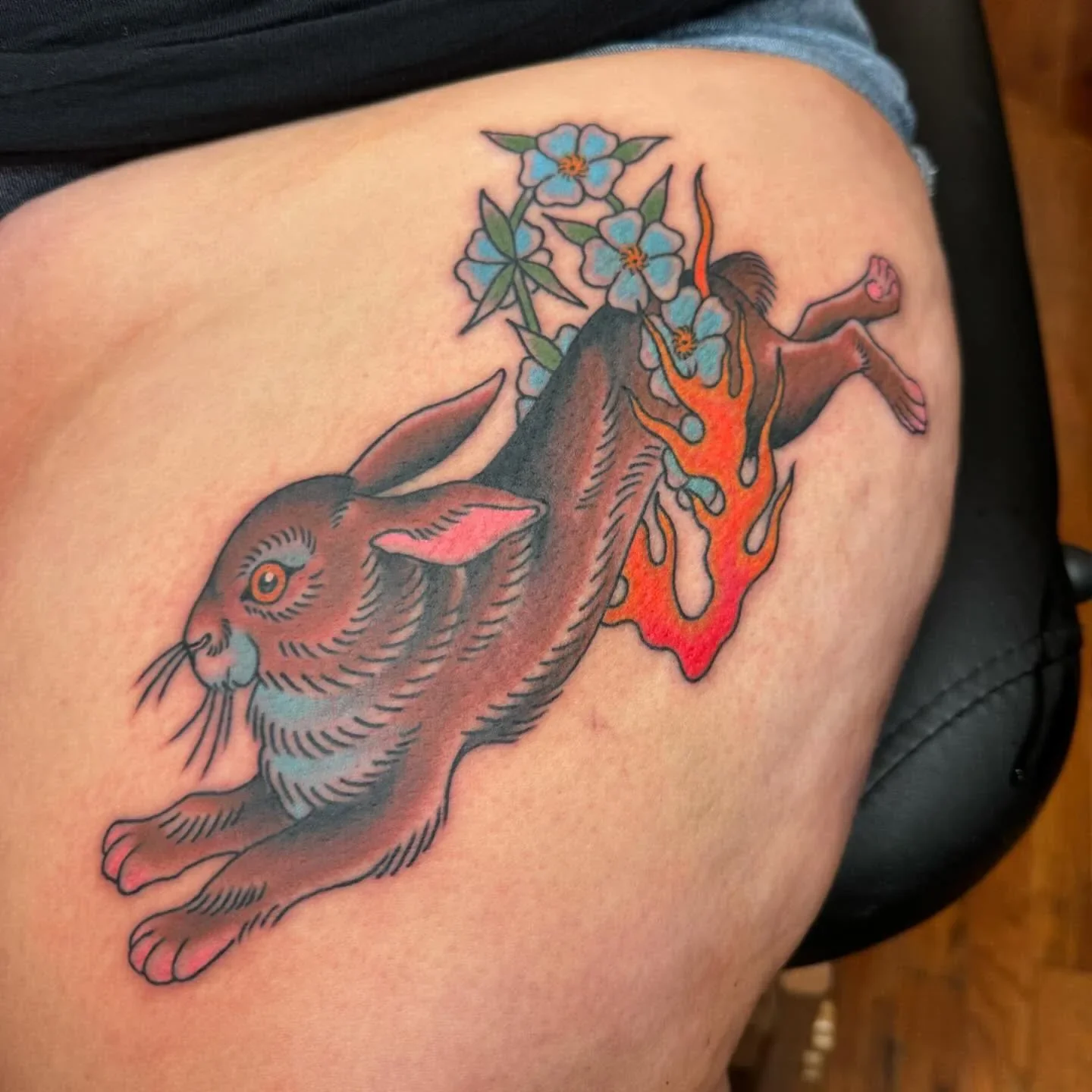 Traditional tattoo of a leaping brown rabbit on fire with light blue flowers. Bold color traditional animal tattoo with surreal flame detail by Brett Semrick.
