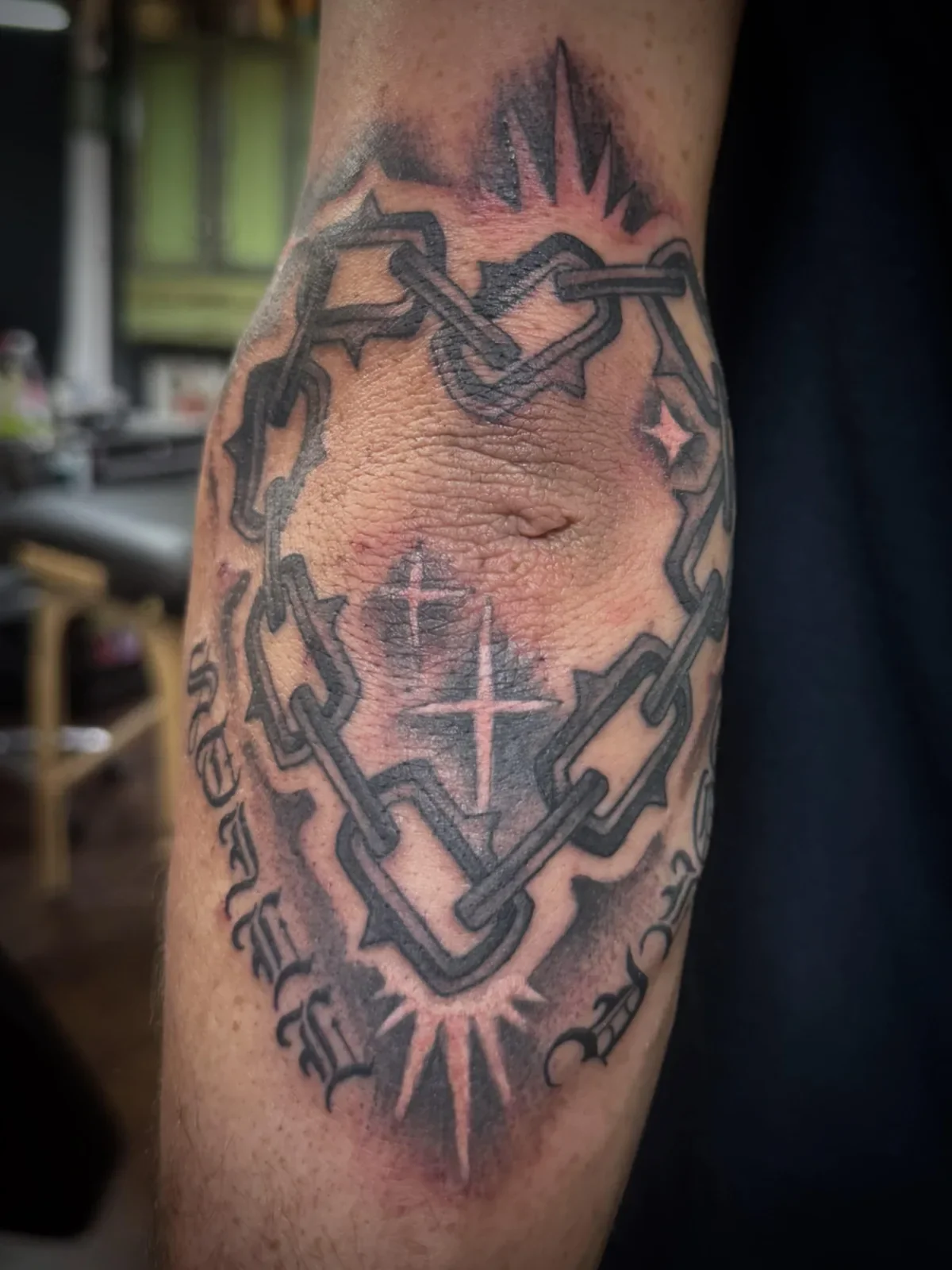 Bold blackwork spiked chain link tattoo wrapping around knee with starbursts and dotwork shading. Heavy illustrative piece with gothic script accents by Brett Semrick in San Diego.