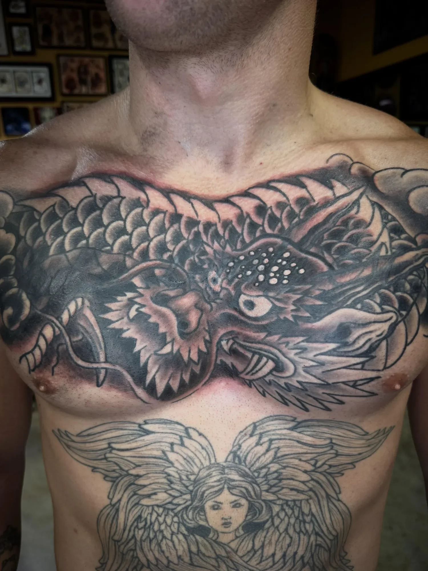 Close-up of a tattoo on a person's chest, featuring a detailed dragon intertwined with a woman's face, with intricate line work and shading.