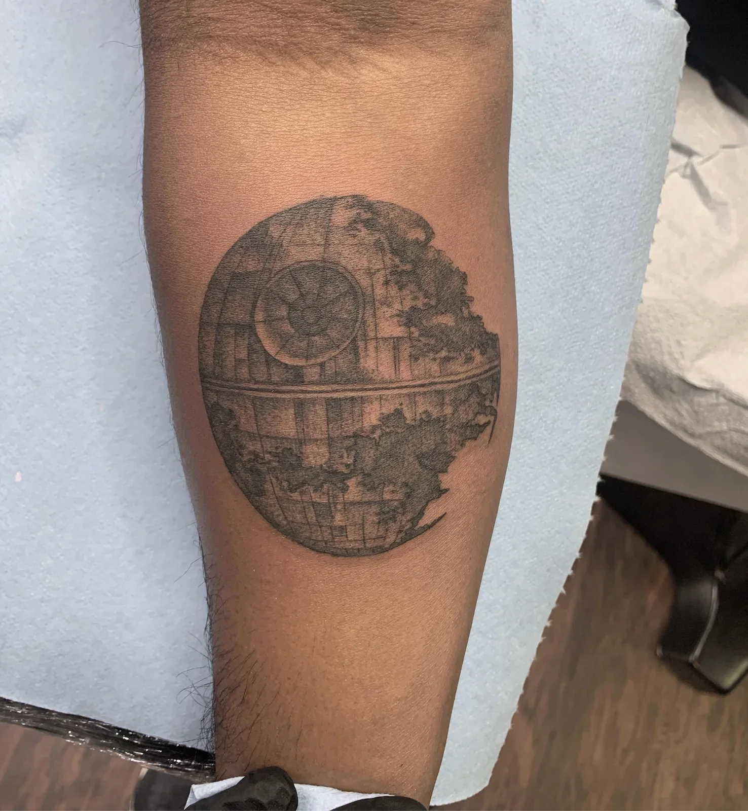 Pop-culture trad — Death Star rendered with forest/terrain texture inside, dotwork and fine line detail.

