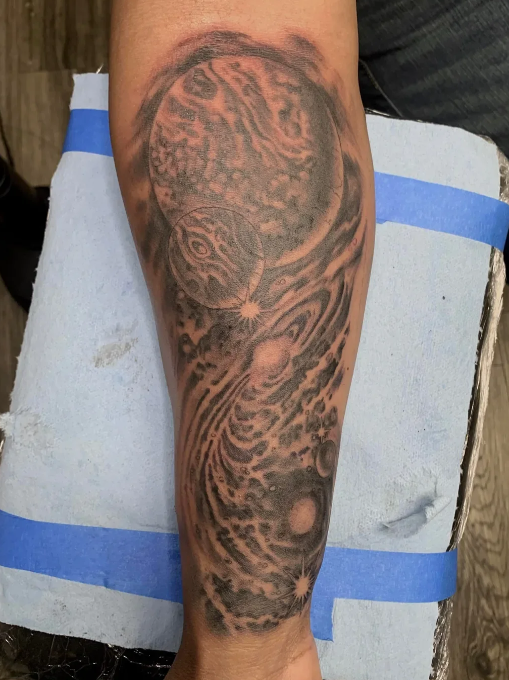 Full forearm black and gray galaxy tattoo featuring detailed planets, Saturn's rings, stars and nebula swirls. Deep space realism by Brett Semrick in San Diego.