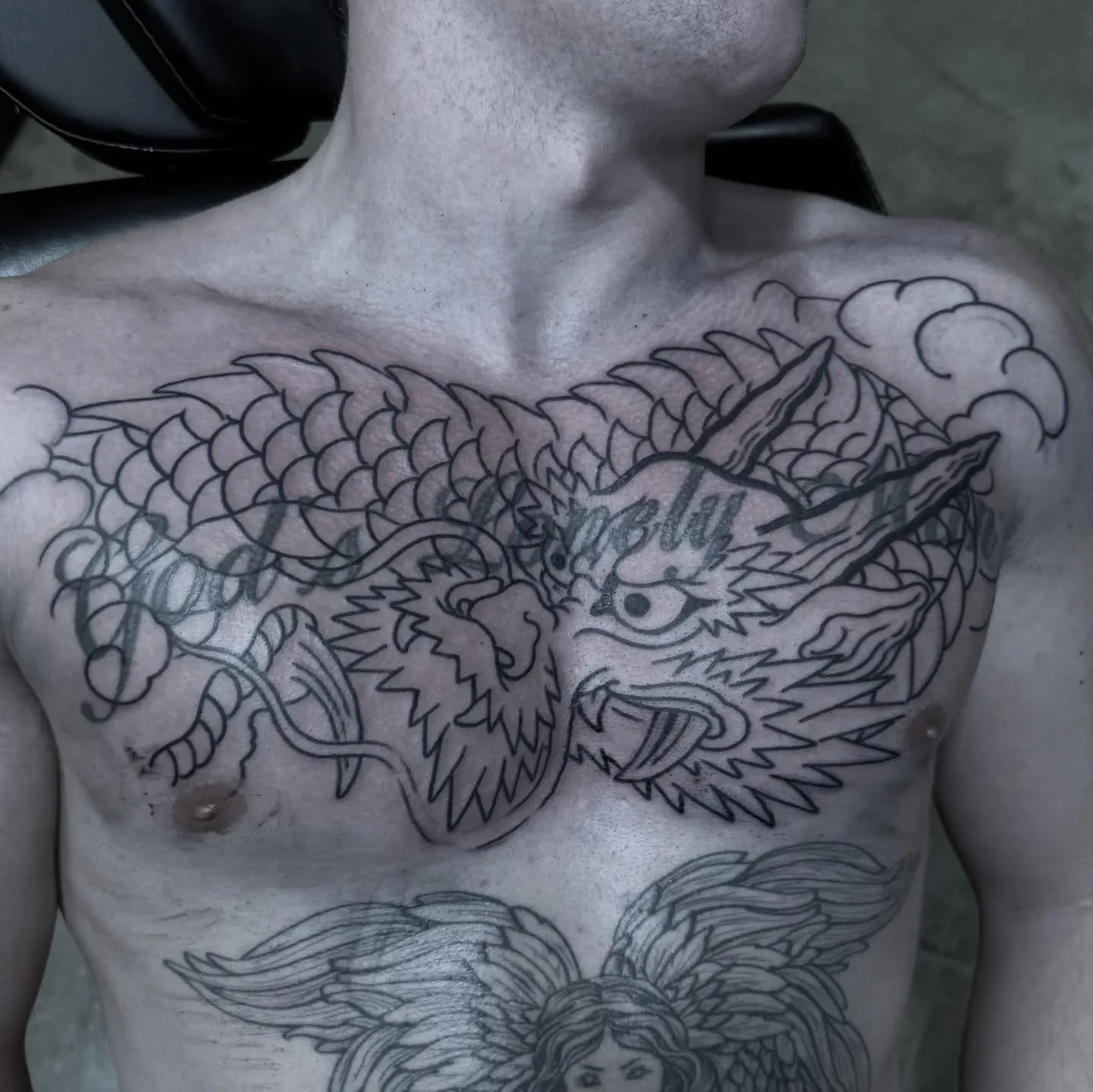 A person's chest with a tattoo of a dragon and a woman with flowing hair, surrounded by clouds.