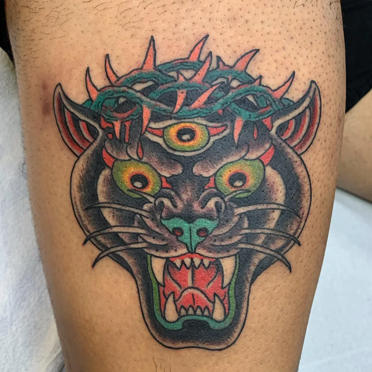 Neo-traditional three-eyed black panther tattoo wearing crown of thorns. Bold color, surreal traditional design by Brett Semrick in San Diego.