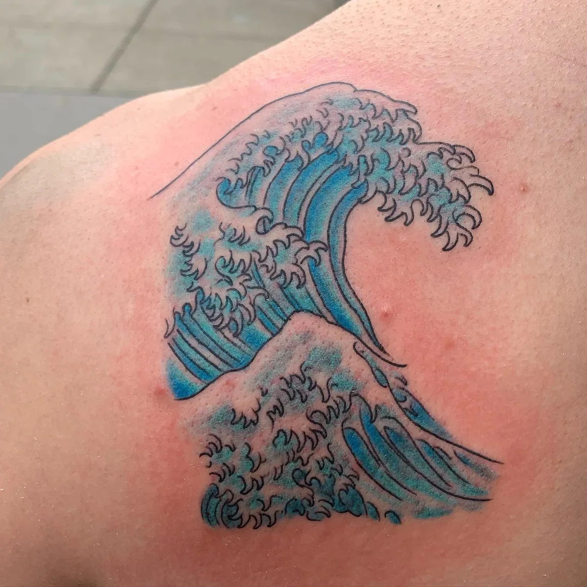 Tattoo of a stylized ocean wave in blue and black ink on skin.