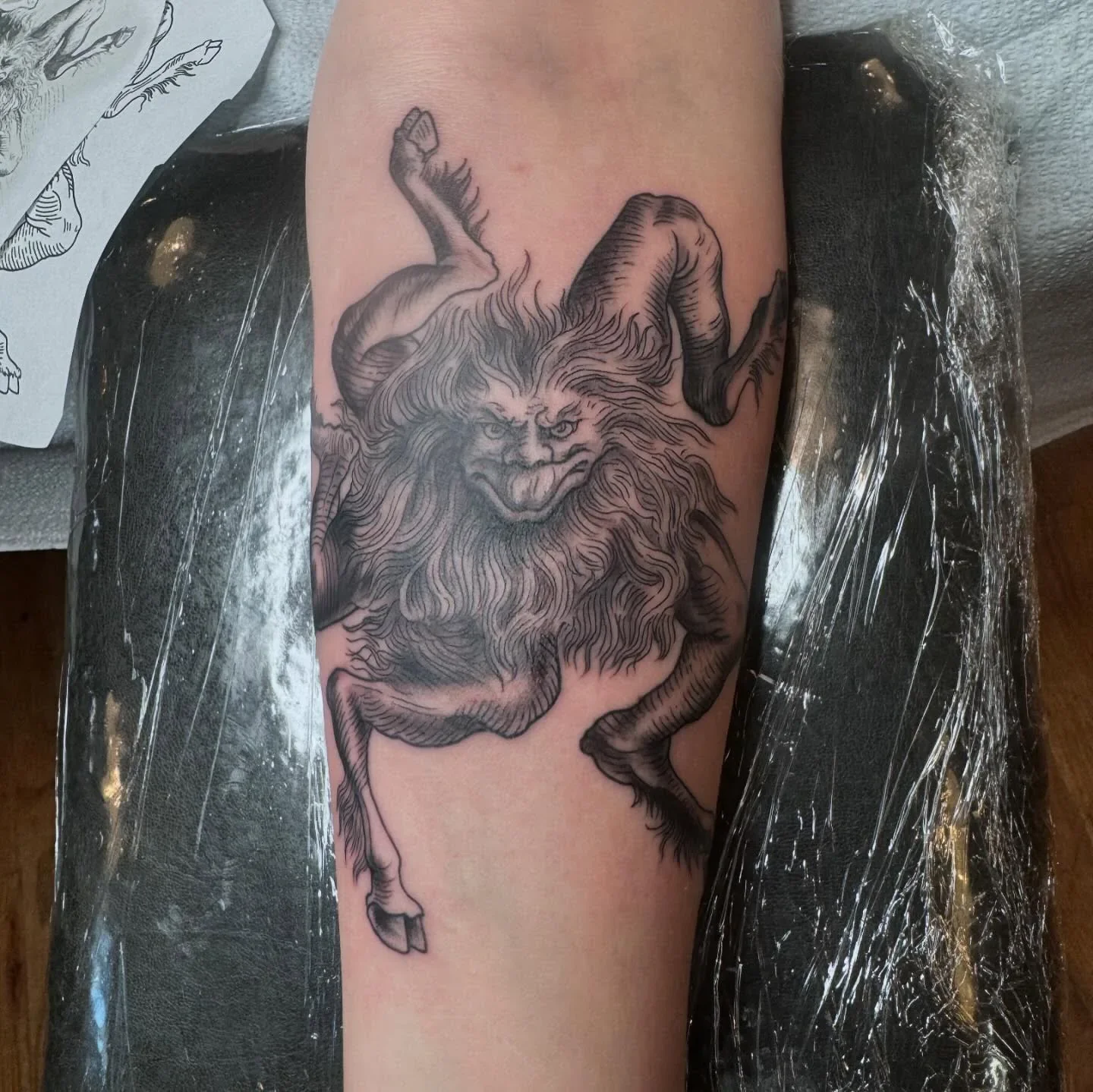 	Detailed blackwork satyr demon tattoo resembling Krampus with ram horns, wild fur beard and cloven hooves in fine etching and woodcut linework style by Brett Semrick.